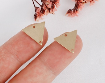 May include: Two gold triangle shaped metal charms with two holes each. The charms are on a finger.