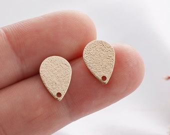May include: Two gold-colored teardrop-shaped metal charms with a small hole at the bottom. The charms have a textured surface.