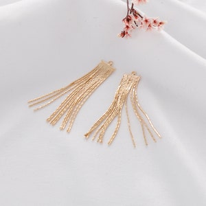 May include: Two gold tassel charms with a loop at the top. The tassels are made of thin, linked chains.