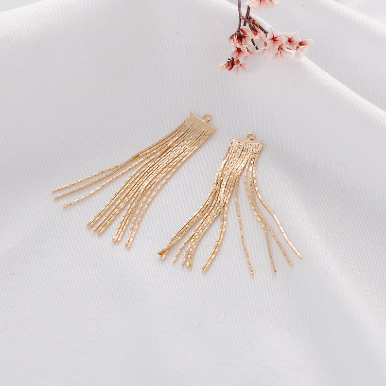 May include: Two gold tassel charms with a loop at the top. The tassels are made of thin, linked chains.