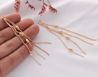 May include: A pair of gold dangle earrings with multiple chains and oval-shaped beads.