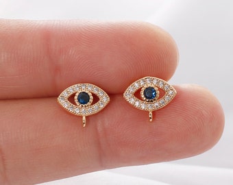May include: A pair of gold-tone earrings with a blue evil eye design. The earrings are adorned with clear cubic zirconia stones.
