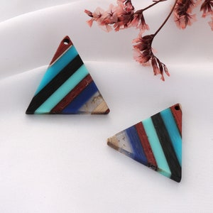 Peut inclure: Deux pendentifs en résine triangulaires avec un design en couches de rayures bleues, turquoise, noires, rouges et blanches. Les pendentifs ont une texture de bois.
