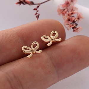 May include: A pair of gold bow-shaped earrings. The earrings are small and delicate, and they are perfect for adding a touch of elegance to any outfit.