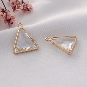 May include: Two gold-toned triangle-shaped pendants with clear glass inserts. The pendants have a loop at the top for attaching to a chain or cord.