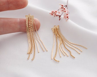 May include: A pair of gold-toned dangle earrings with multiple chains and beads. The earrings are on a white surface.
