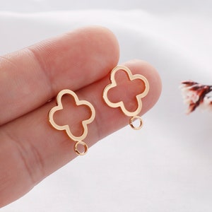 May include: A pair of gold-tone metal earrings with a four-leaf clover design. Each earring has a small loop at the bottom.