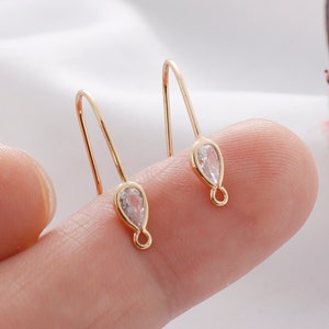 May include: A pair of gold-tone dangle earrings with a teardrop-shaped clear crystal at the end of each earring.