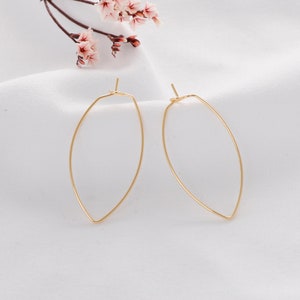 May include: A pair of gold-toned, oval-shaped hoop earrings. The earrings are made of thin wire and have a simple, minimalist design.