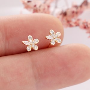 May include: A pair of gold flower-shaped earrings with clear cubic zirconia stones.