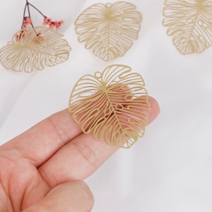 May include: Gold metal leaf charms with a delicate, intricate design. The leaves have a cutout pattern and are perfect for jewelry making or crafting projects.