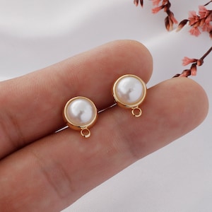 May include: Two gold-toned earring findings with a white pearl in the center. Each finding has a small loop at the bottom.