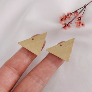 May include: Two gold triangle-shaped earring blanks with a small hole in the center of each triangle.