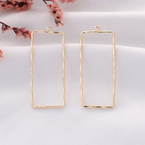 May include: Two gold-toned rectangular earring blanks with a loop at the top. The blanks are smooth and have a slightly textured finish.
