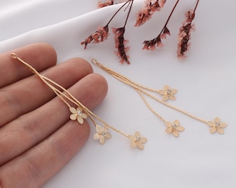 May include: A pair of gold dangle earrings with a delicate chain and multiple flower charms. Each flower charm has a small rhinestone in the center.