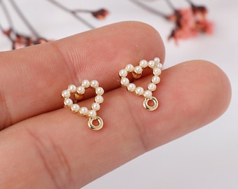 May include: A pair of gold heart-shaped earring charms with a pearl border and a small gold loop hanging from the bottom.