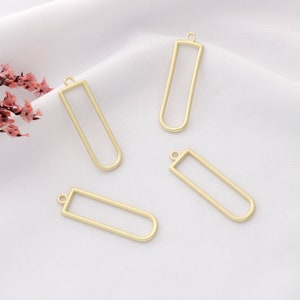 May include: Four gold-colored metal pendant frames in the shape of a rectangle with rounded corners. The frames are approximately 2 inches long and 1 inch wide.
