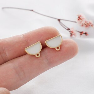 May include: Two gold-toned half-circle earrings with white enamel. The earrings have a loop at the bottom for attaching to a hook.