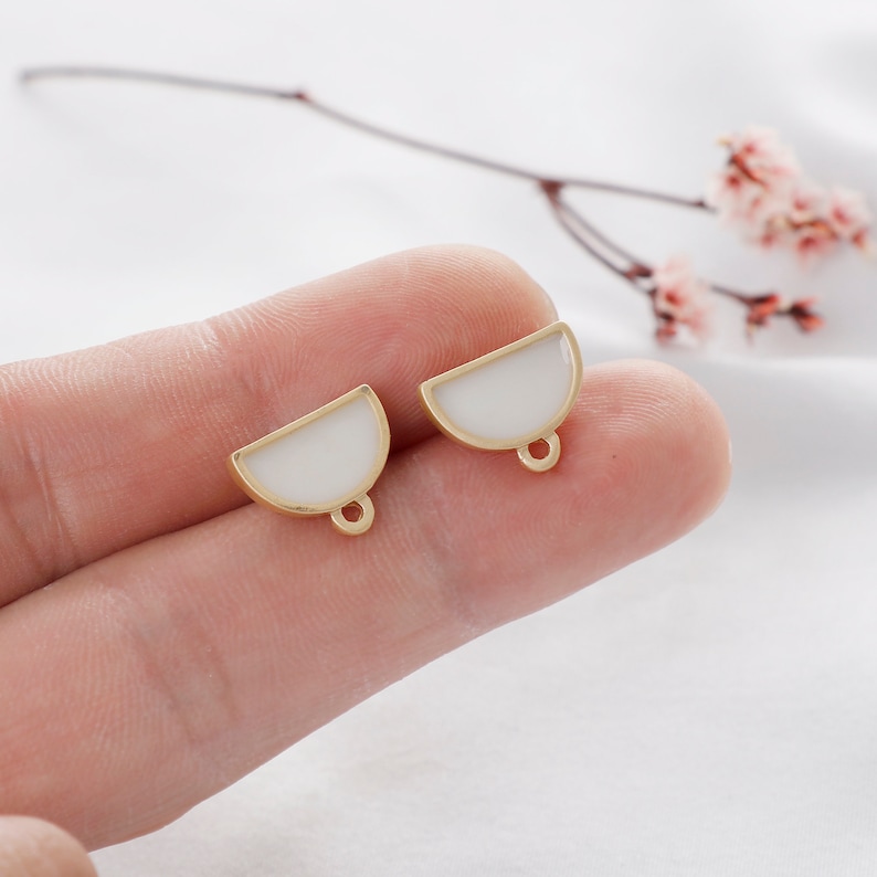 May include: Two gold-toned half-circle earrings with white enamel. The earrings have a loop at the bottom for attaching to a hook.