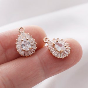 May include: Two gold-tone teardrop-shaped charms with clear cubic zirconia stones. The stones are surrounded by smaller clear cubic zirconia stones.