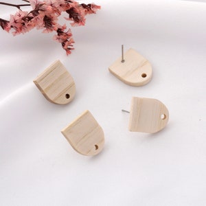 May include: Four unfinished wooden earrings with a small hole at the top. The earrings are shaped like a rounded rectangle.