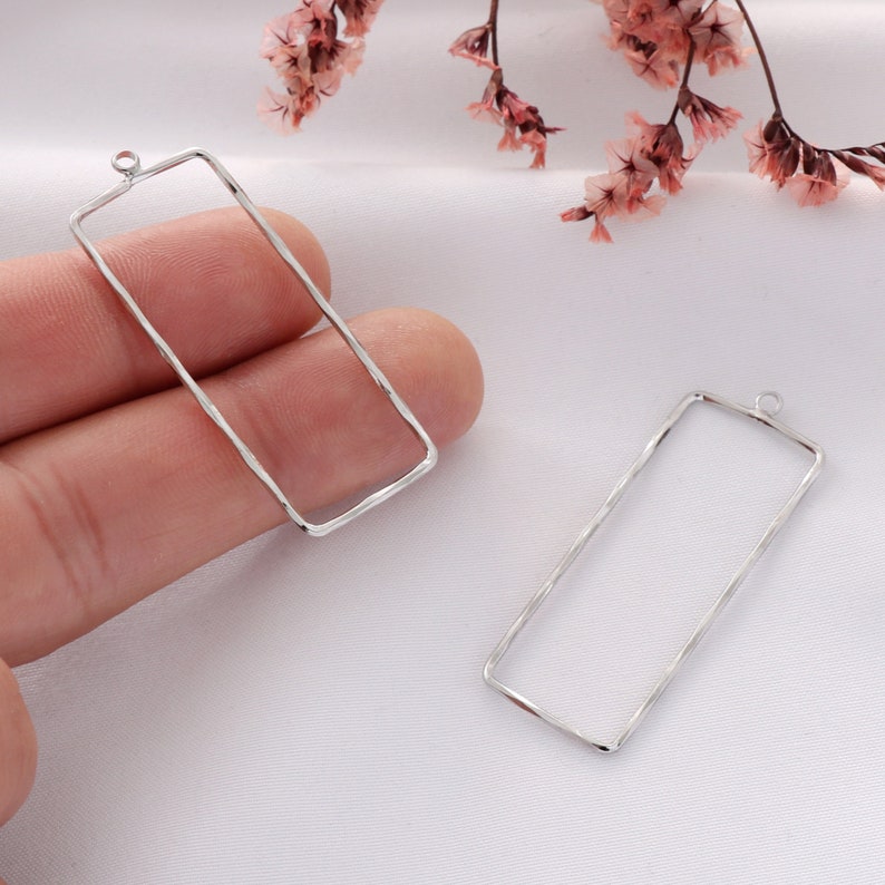 Op de afbeelding: Twee rechthoekige metalen frames in zilver met een textuur. Elk frame heeft een kleine lus aan de bovenkant om op te hangen.