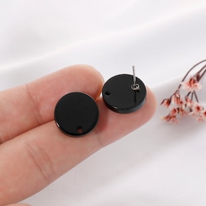 May include: A pair of black round stud earrings with a small hole in the center of each earring.