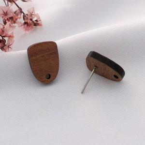 May include: A pair of wooden earrings with a natural wood grain finish. The earrings are shaped like a rounded rectangle and have a small hole in the top for the post. The earrings are shown on a white background.