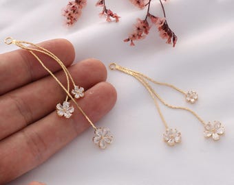 May include: A pair of gold dangle earrings with three flower-shaped charms on each earring. The charms are made of clear rhinestones.