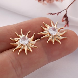 May include: A pair of gold-tone earrings with a sunburst design and clear crystal center stones.