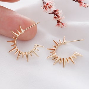 May include: A pair of gold-toned hoop earrings with a pointed starburst design. The earrings are small and delicate.