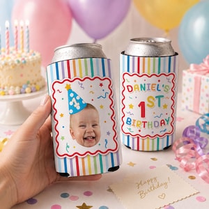 May include: Two cylindrical foam can coolers featuring a vertical rainbow stripe pattern. One cooler displays a photograph of a smiling baby wearing a blue party hat with a number one. The other cooler features the text Daniel's 1st Birthday.