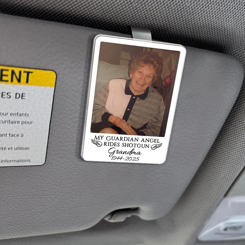 May include: A rectangular car visor accessory with a photo of an elderly woman. The text "MY GUARDIAN ANGEL RIDES SHOTGUN Grandma 1944-2025" is printed below the photo. The accessory is attached to a car visor.