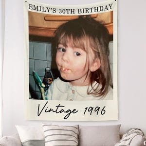 May include: A cream-colored wall tapestry featuring a vintage photo of a young person. The text "EMILY'S 30TH BIRTHDAY" is at the top, with "Vintage 1996" at the bottom. The photo shows a person with food on their face.