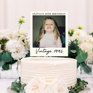 K&ouml;nnte beinhalten: Ein rechteckiger Tortenaufleger mit einem Foto eines jungen Kindes mit langem blonden Haar. Der Text OLIVIA'S 30TH BIRTHDAY ist oben aufgedruckt und der Text Vintage 1996 ist unten in einer schwarzen Schreibschrift zu sehen.