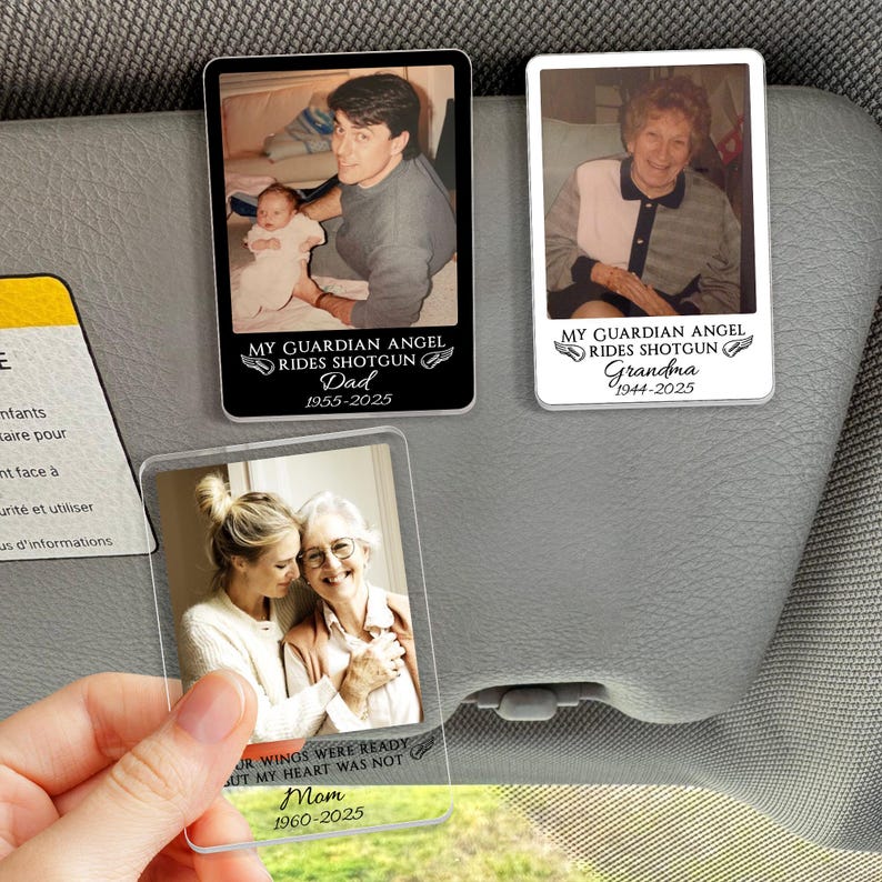 May include: Three rectangular car visor clips with photos of loved ones. One clip has a photo of a man holding a baby, with the text "MY GUARDIAN ANGEL RIDES SHOTGUN Dad 1955-2025". Another clip has a photo of a woman, with the text "Grandma 1944-2025". The third clip has a photo of two women, with the text "Mom 1960-2025".