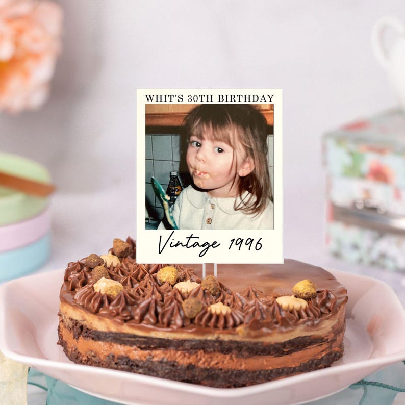 K&ouml;nnte beinhalten: Ein runder Schokoladenkuchen mit aufgespritzter Creme und kleinen Keksst&uuml;cken, verziert mit einem rechteckigen Tortenstecker, der ein Kinderfoto im Vintage-Stil sowie den Text "WHIT'S 30TH BIRTHDAY" und "Vintage 1996" auf dem Rand zeigt.
