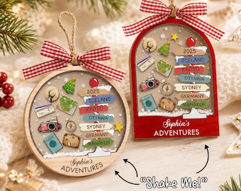 May include: Two wooden ornaments, one round and one arched, featuring travel-themed icons like a camera, passport, and map. Each has a red and white gingham bow, a signpost with locations like Iceland and Kyoto, and the text Sophia's ADVENTURES.