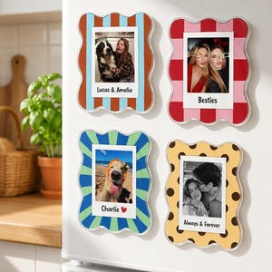 May include: Four rectangular magnetic photo frames with wavy edges. The top left frame has blue and orange stripes with the text Lucas & Amelia. The top right frame has red and pink checks with the text Besties. The bottom left has blue and green stripes with the text Charlie. The bottom right has yellow with brown dots and the text Always & Forever.
