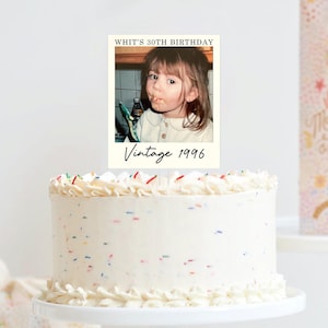 K&ouml;nnte beinhalten: Ein runder wei&szlig;er Kuchen mit bunten Streuseln, gekr&ouml;nt von einer rechteckigen Karte mit dem Foto eines kleinen Kindes. Der Text auf der Karte lautet oben WHIT'S 30TH BIRTHDAY und unten Vintage 1996 in einer schwarzen Schreibschrift.