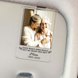 May include: Clear acrylic memorial photo holder with a picture of two women. The holder has the text "YOUR WINGS WERE READY BUT MY HEART WAS NOT Mom 1960-2025" in black script and a pair of wings.