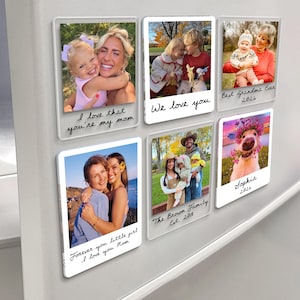 May include: A collection of clear acrylic photo magnets, each displaying a different family photo. Handwritten text includes phrases like "I love that you're my mom" and "Best Grandma Ever 2026". The photos feature people and a dog.