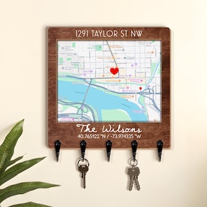 May include: A square wooden wall-mounted key holder featuring a printed map with a red heart icon. The top text reads 1291 TAYLOR ST NW, and the bottom text reads The Wilsons followed by the coordinates 40.765122 N / -73.974335 W. Five black hooks.