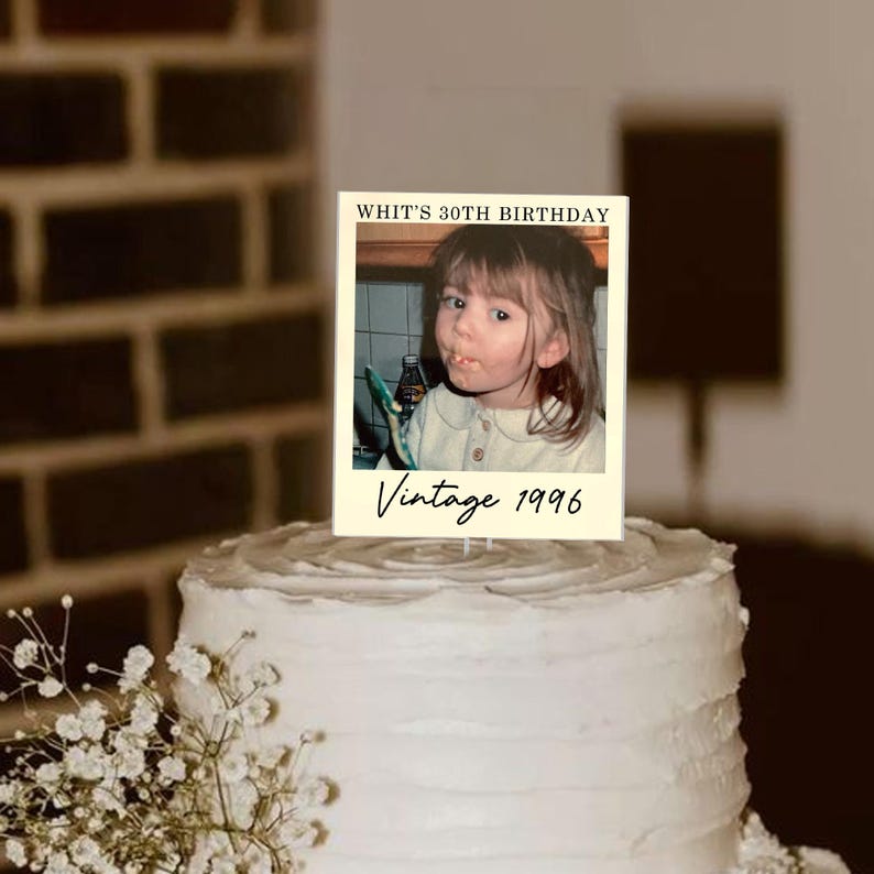 K&ouml;nnte beinhalten: Ein rechteckiger Tortenaufleger mit einem Foto eines Kindes, dem Text "WHIT'S 30TH BIRTHDAY" oben und "Vintage 1996" in Schreibschrift unten. Der Aufleger befindet sich auf einer wei&szlig; glasierten Torte mit einer strukturierten Oberfl&auml;che.