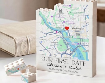 May include: A white building block display featuring a map of Washington D.C. with a red heart icon. The text reads OUR FIRST DATE, Ederson + Violet, and the coordinates 38.884535 N / -77.069315 W. Two smaller matching blocks are placed in the foreground.