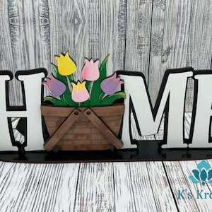 May include: Wooden home sign with the word "HOME" in white letters with black outlines. The sign features a basket of colorful tulips in shades of pink, purple, yellow, and green.