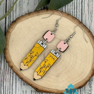 May include: A pair of yellow pencil-shaped earrings with pink accents. The earrings feature a sun and flowers on one side and the word "grow" on the other.