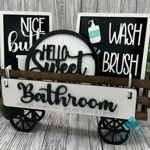 May include: A wooden wagon with black wheels and white signs. The signs say "Nice But", "Hello Sweet", "Wash Brush", and "Bathroom Open 24 Hours - Please Seat Yourself".