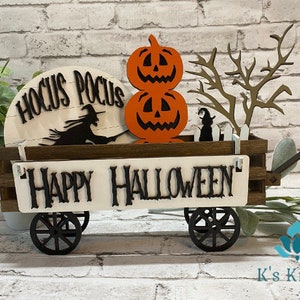 May include: A wooden wagon decorated for Halloween with a "Hocus Pocus" sign, a witch on a broomstick, two jack-o'-lantern pumpkins, a spooky tree, and a sign that reads "Happy Halloween".