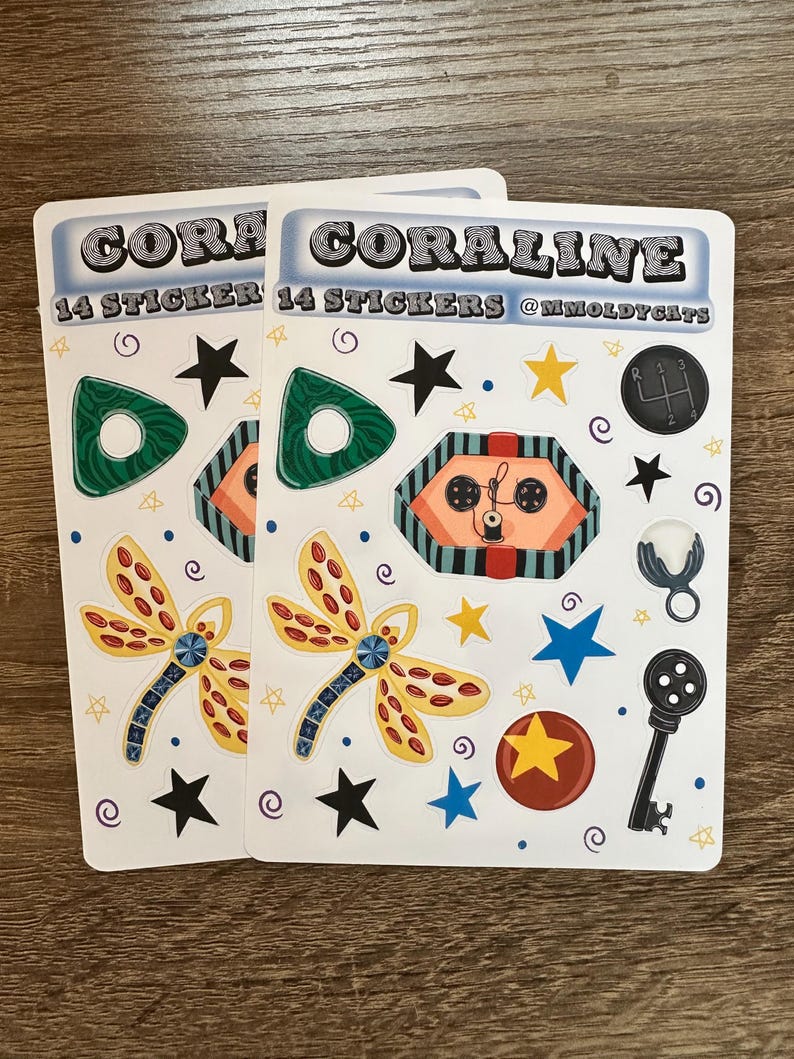 May include: Two sticker sheets with the word "CORALINE" and "14 STICKERS" printed on them. The stickers feature a variety of designs, including a dragonfly, stars, a key, and a gear shift. The stickers are in various colors, including green, orange, yellow, blue, and black.